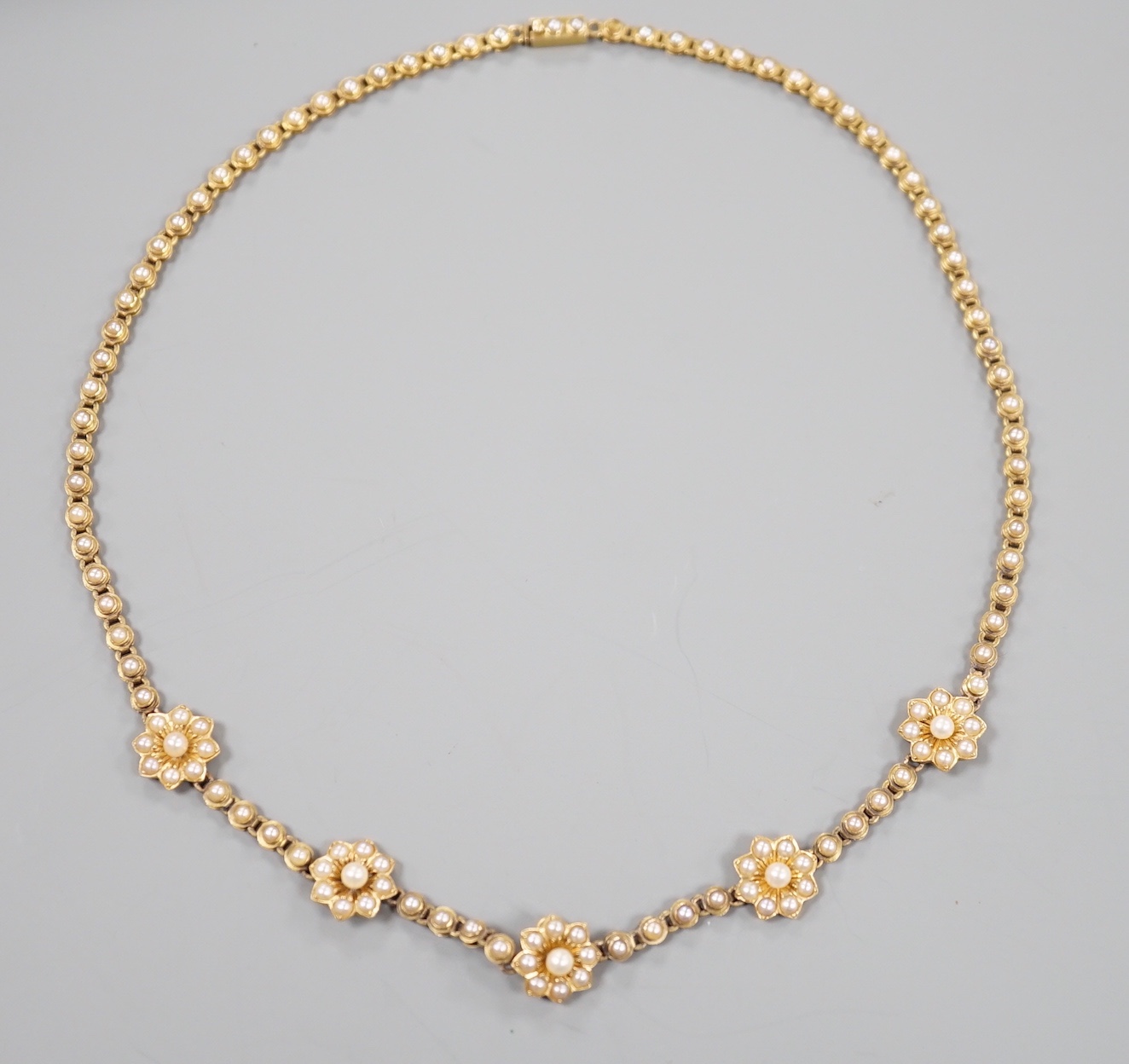 A late Victorian yellow metal and seed pearl set flower head motif necklace, (lacking drop pendant), 36cm, gross weight 18 grams.